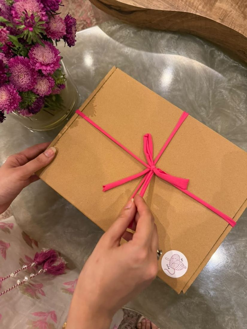 Hands tying a kraft box with pink t-shirt yarn
