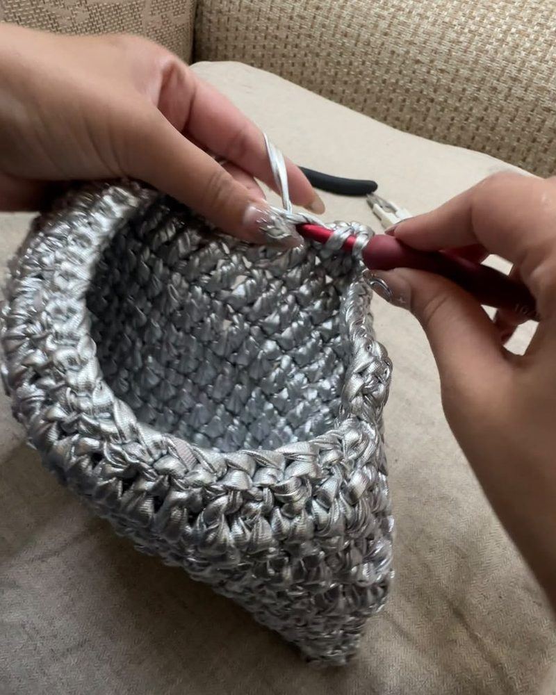 Hands crocheting a silver bag