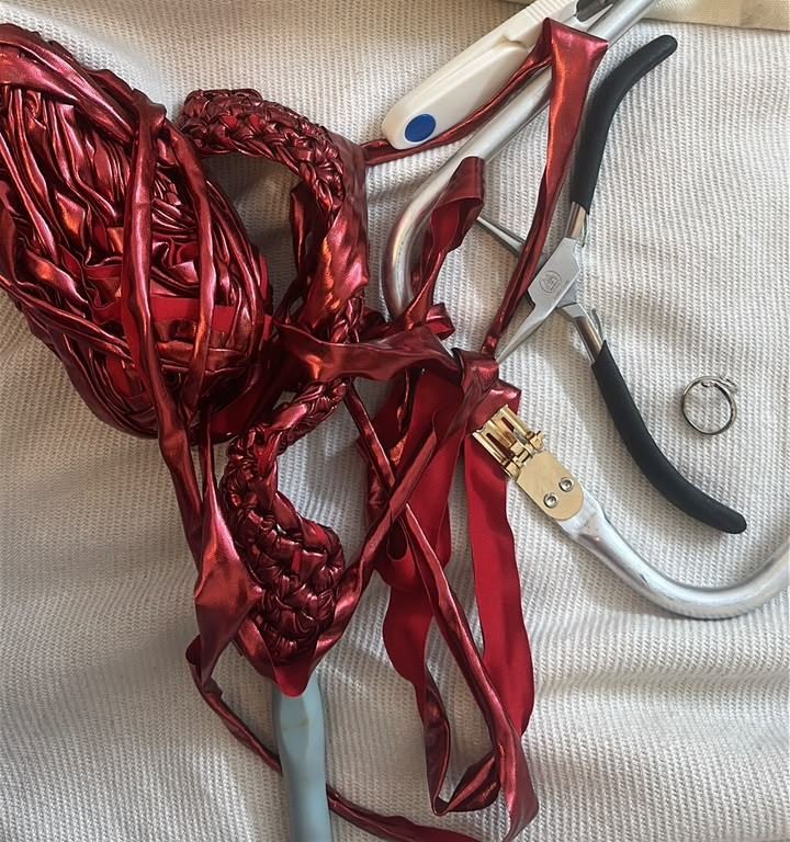 Red metallic yarn, a braided strap in progress, crochet hook, pliers and snips