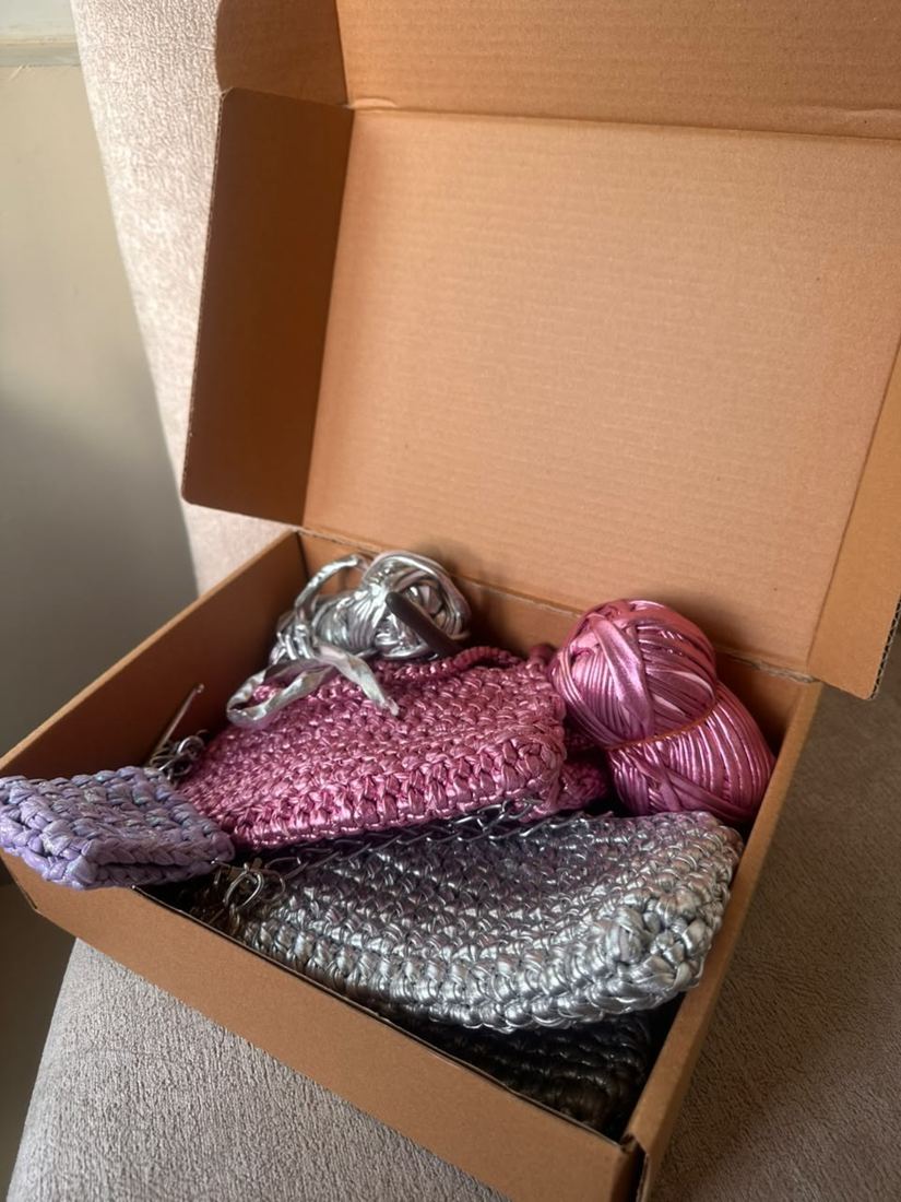 A box of metallic t-shirt yarn balls with a crochet hook and half-made bags